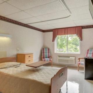 A hospital room with a bed, chairs, and a window providing natural light.