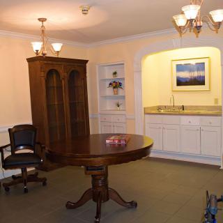 A well-furnished office space featuring a round wooden table, an office chair, a tall cabinet, and built-in shelving with overhead lighting.