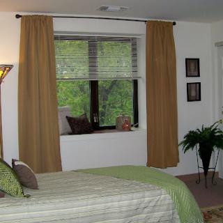 A cozy bedroom with green bedding and warm curtains, featuring a window view.