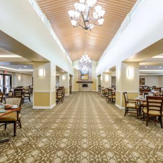 A spacious and elegantly designed dining hall with chandeliers, tables, and chairs arranged neatly on a patterned carpet.