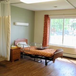 A hospital room with a single bed, nightstand, and large window.