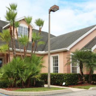 A suburban house with palm trees and well-manicured landscaping.
