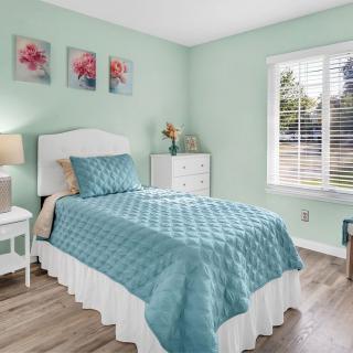 A cozy bedroom with a single bed covered in blue bedding, complemented by floral wall decor and a view of the outside through the window.