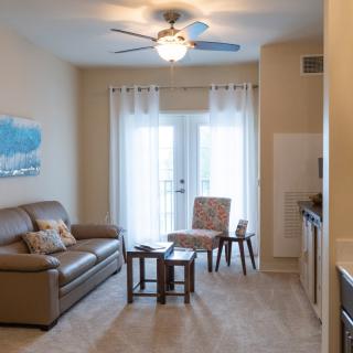 A cozy living room with a sofa, table, and chairs, featuring a ceiling fan and artwork on the wall.
