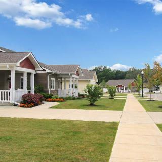 A peaceful suburban neighborhood with houses, a sidewalk, and well-maintained lawns under a clear blue sky.