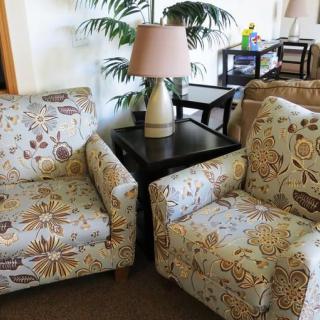 A cozy living room setup with two floral patterned chairs, a lamp on a side table, and indoor plants.