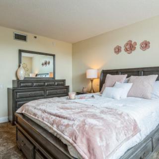 A cozy bedroom with a neatly made bed, decorative pillows, a bedside lamp, and a dresser with a mirror.