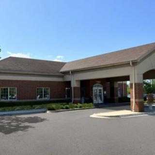 A one-story building with a covered entrance and a brick exterior sits adjacent to an empty parking lot on a clear day.