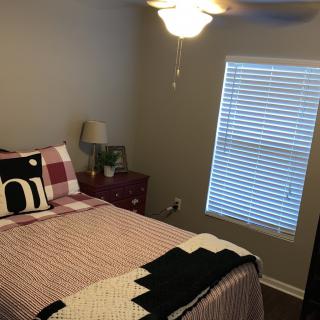 A cozy bedroom with a neatly made bed, a bedside lamp, and a window with blinds.