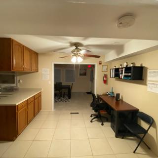 A cozy kitchen and workspace area with cabinets, a desk, and a ceiling fan.