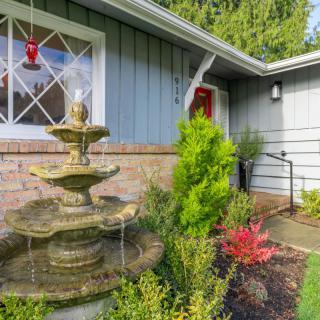 A picturesque front yard featuring a multi-tiered fountain set against a well-manicured garden and house exterior.