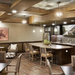 A modern restaurant interior featuring a bar counter with wooden chairs, stylish lighting fixtures, and contemporary decor.
