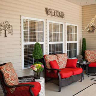 A cozy patio setup with wicker furniture and vibrant red cushions, adorned with decorative elements and a welcome sign.