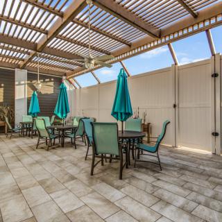 A covered patio area with tables, chairs, and umbrellas under a pergola.