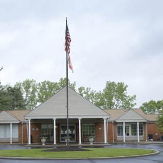 A single-story building with an American flag at the entrance, surrounded by trees under an overcast sky.