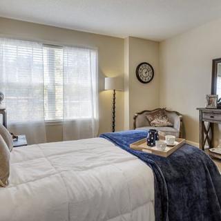 A cozy bedroom with elegant decor featuring a neatly made bed, a plush armchair, and tasteful furnishings including a lamp and mirror.