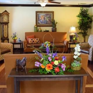 A cozy living room featuring elegant furniture, a grandfather clock, and vibrant floral arrangements.