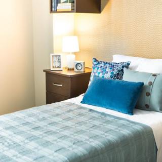 A cozy bedroom with a neatly made bed adorned with colorful pillows and a bedside table featuring a lamp and photo frame.