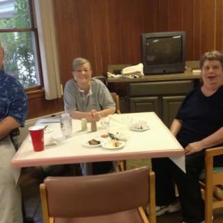 A group of people sitting around a dining table in a room with a television in the background.
