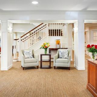 A spacious living room featuring two armchairs, a small table with flowers, and a staircase in the background.