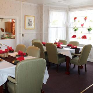 A cozy dining room with neatly set tables and comfortable chairs, adorned with floral decorations by the windows.