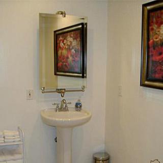 A small bathroom with a pedestal sink, mirror, and framed artwork on the walls.