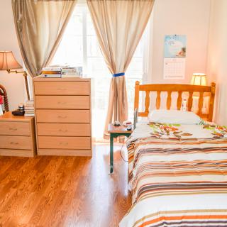A cozy bedroom with a single bed, wooden floor, and ample natural light.