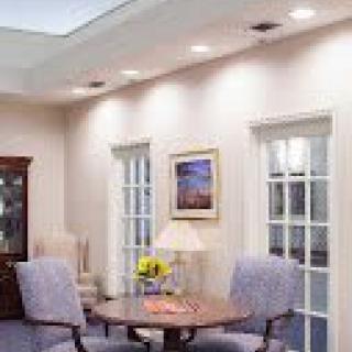 A cozy meeting room with a round table and upholstered chairs, decorated with a painting and lamps.