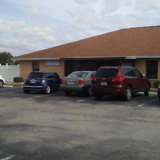 A view of a parking lot with several cars parked in front of a building under a cloudy sky.