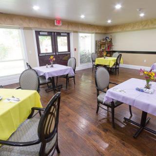 A cozy dining area with neatly set tables, each adorned with colorful tablecloths and fresh flower arrangements.