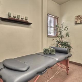 A tranquil spa room featuring a massage table, neatly rolled towels, candles, and a decorative plant.