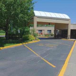 A building with a covered entryway and landscaped driveway on a sunny day.