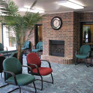 A cozy waiting room with a brick fireplace, clock, chairs, and an indoor plant.