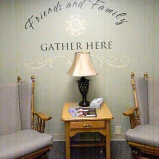 A cozy seating area with two chairs, a lamp, and a side table under a sign that reads 'Friends and Family Gather Here'.