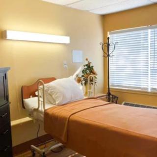A clean and well-lit hospital room featuring a single bed and a window with blinds.