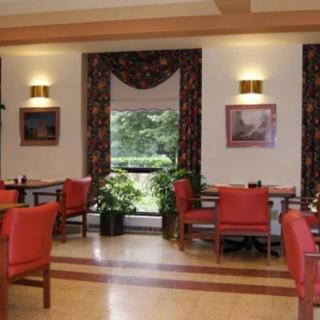 A cozy dining room with red chairs, tables, and a large window overlooking greenery.