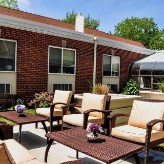 A cozy patio with comfortable seating and tables adorned with flowers, set against a brick building on a sunny day.