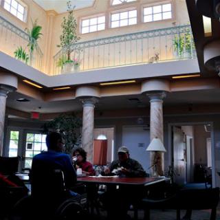 A cozy lobby area featuring columns, natural light streaming in from the upper level, and people gathered around a table.