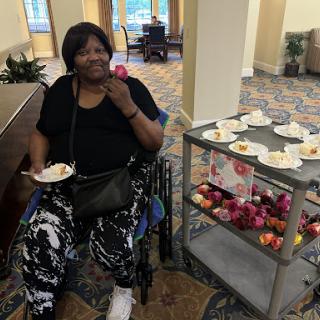 A joyful woman enjoying a treat at a social gathering, seated in her wheelchair beside a food cart filled with snacks.