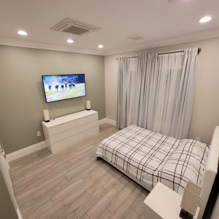 A modern, minimalist bedroom featuring a wall-mounted television and a neatly arranged bed.