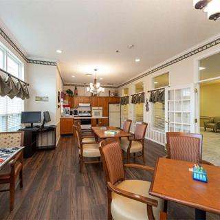 A spacious kitchen and dining area featuring wood flooring, multiple tables and chairs, ample windows, and a computer desk.