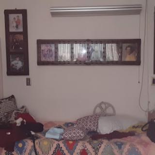 A cozy yet cluttered room featuring a bed, shelves of books or items, and decorative blankets.