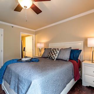 A cozy bedroom with a neatly made bed, ceiling fan, and warm lighting from bedside lamps.
