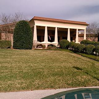 A picturesque building with columns and manicured landscaping, set against a cloudy sky.