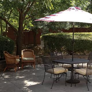 A peaceful patio area with a table and chairs under a large umbrella, surrounded by lush greenery.