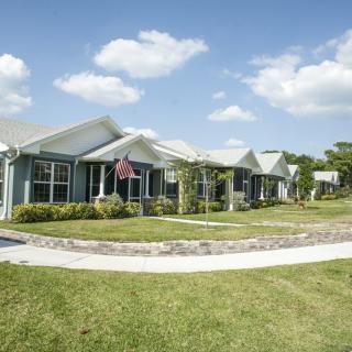 A row of suburban houses with well-maintained lawns and a curved pathway under a partly cloudy sky.