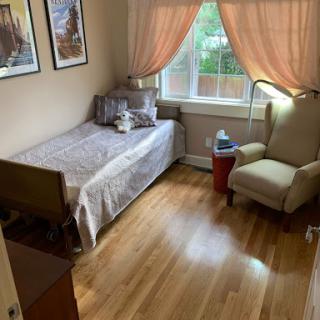 A cozy bedroom featuring a single bed, an armchair, and large windows with soft curtains.