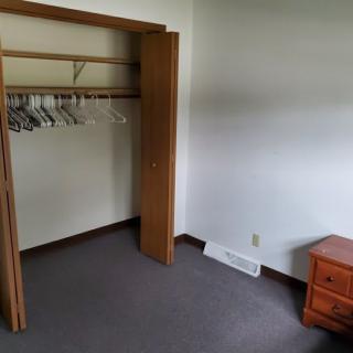 An empty room with an open closet containing hangers and a wooden nightstand.