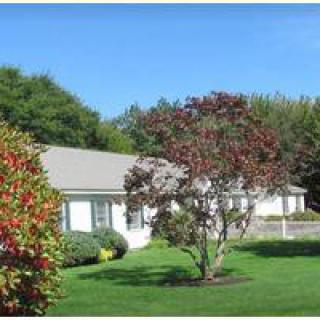 A suburban house with a well-maintained lawn and trees under a clear blue sky.