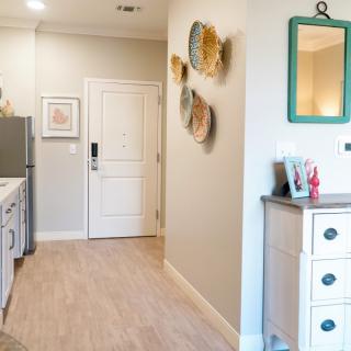 A modern apartment entryway featuring a kitchen with wooden flooring, white cabinetry, and decorative wall art.